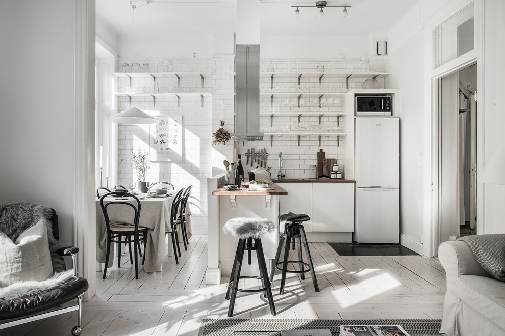 Photo of a scandinavian l-shaped open plan kitchen in Stockholm with open cabinets, wood benchtops, painted wood floors, white floor, white splashback, subway tile splashback, white appliances and a peninsula.