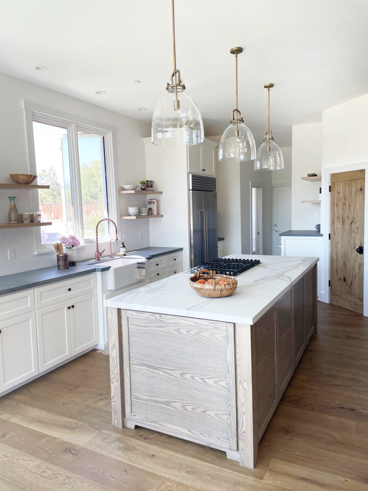 Large farmhouse single-wall medium tone wood floor, brown floor and exposed beam eat-in kitchen photo in Santa Barbara with a farmhouse sink, shaker cabinets, white cabinets, quartz countertops, white backsplash, porcelain backsplash, stainless steel appliances, two islands and white countertops