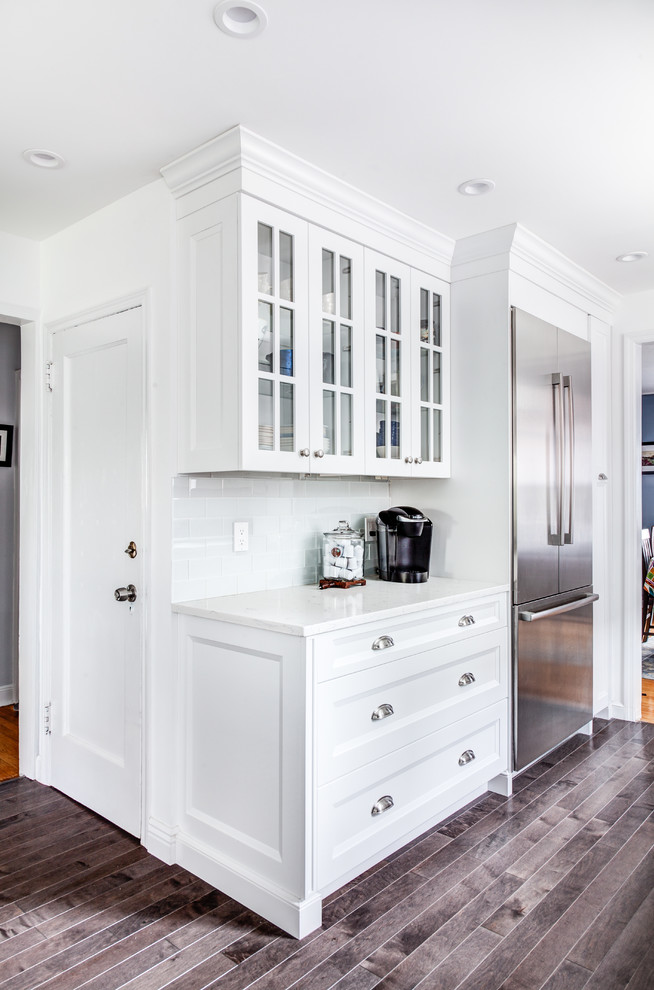Design ideas for a small transitional galley open plan kitchen in New York with white cabinets, quartz benchtops, glass tile splashback, stainless steel appliances, dark hardwood floors, brown floor, an undermount sink, recessed-panel cabinets and white splashback.