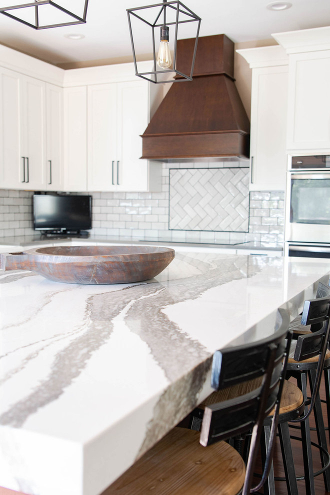 Mid-sized transitional l-shaped medium tone wood floor and brown floor eat-in kitchen photo in Omaha with a farmhouse sink, shaker cabinets, white cabinets, quartzite countertops, white backsplash, subway tile backsplash, stainless steel appliances, an island and white countertops
