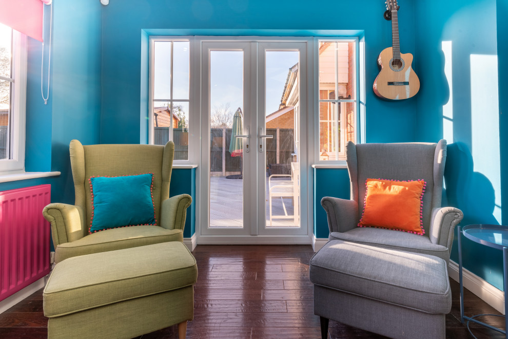 Aménagement d'un grand salon contemporain ouvert avec un mur bleu, parquet foncé, un téléviseur fixé au mur, un sol marron, éclairage et une bibliothèque ou un coin lecture.