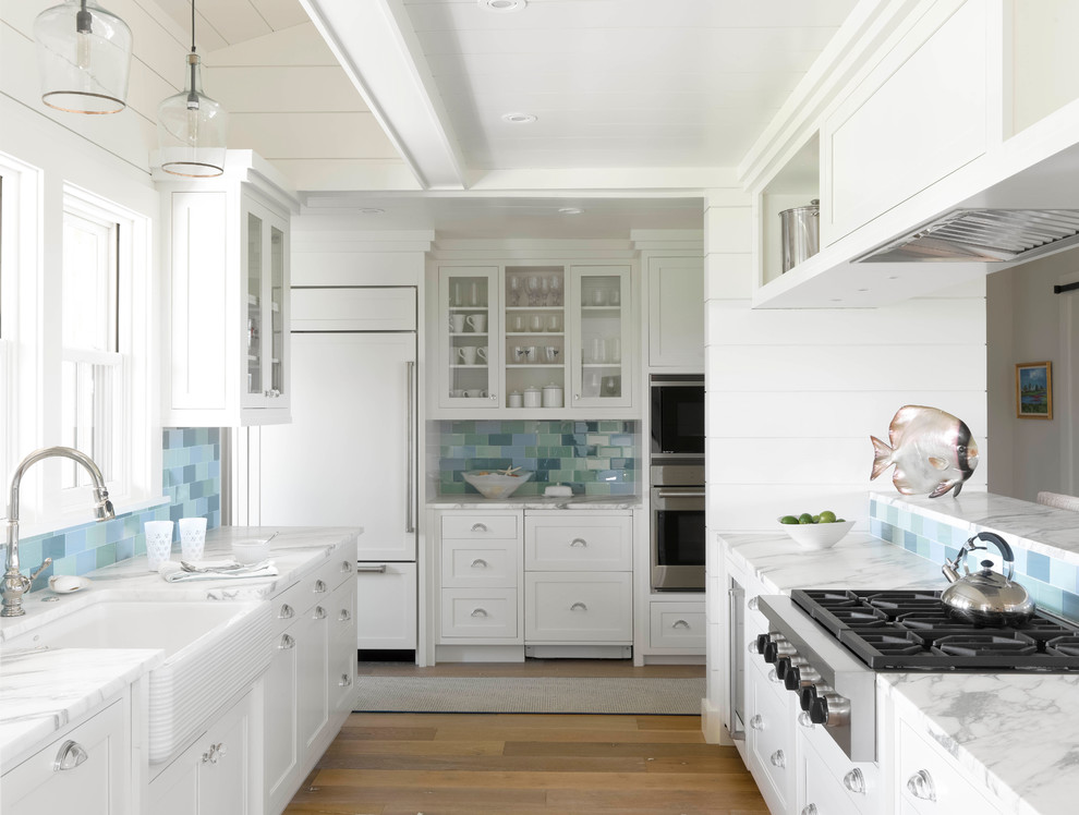 This is an example of a mid-sized beach style kitchen pantry in Boston with a farmhouse sink, shaker cabinets, white cabinets, limestone benchtops, porcelain splashback, white appliances, light hardwood floors, no island, brown floor, multi-coloured benchtop, recessed and blue splashback.