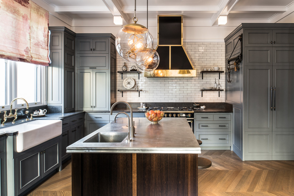 This is an example of a mid-sized transitional l-shaped eat-in kitchen in San Francisco with a farmhouse sink, medium hardwood floors, with island, brown floor, recessed-panel cabinets, grey cabinets, white splashback, panelled appliances and black benchtop.