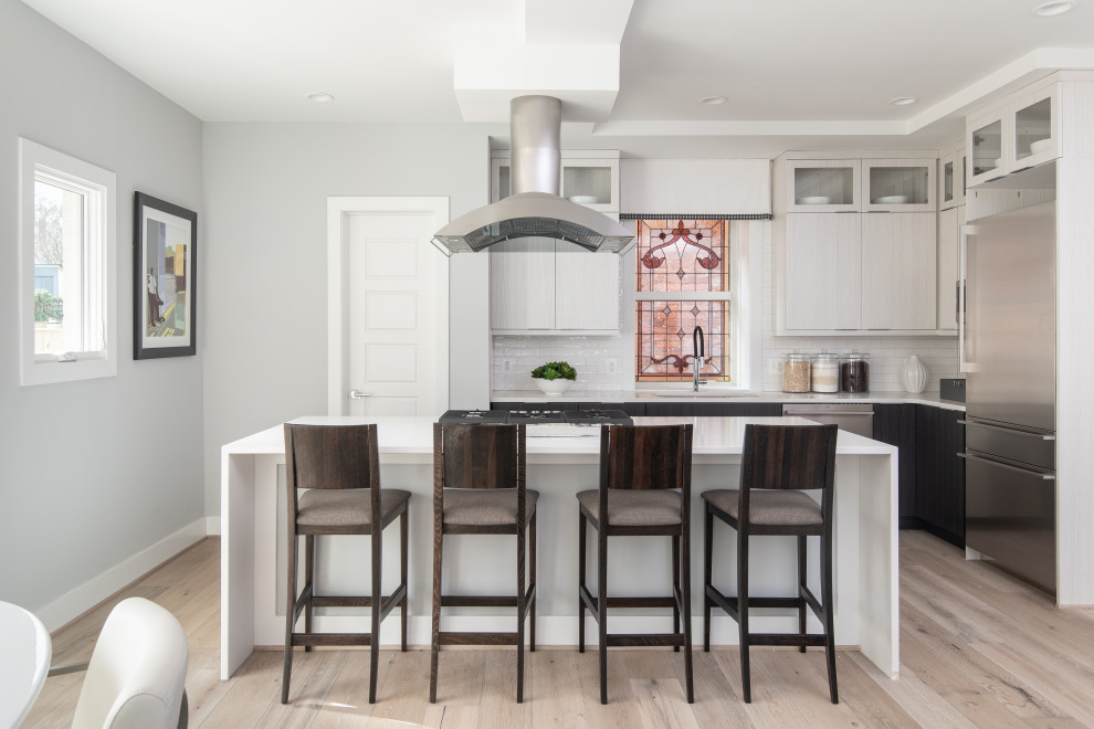 Photo of a transitional l-shaped eat-in kitchen in DC Metro with an undermount sink, flat-panel cabinets, grey cabinets, white splashback, subway tile splashback, stainless steel appliances, light hardwood floors, with island, beige floor and white benchtop.