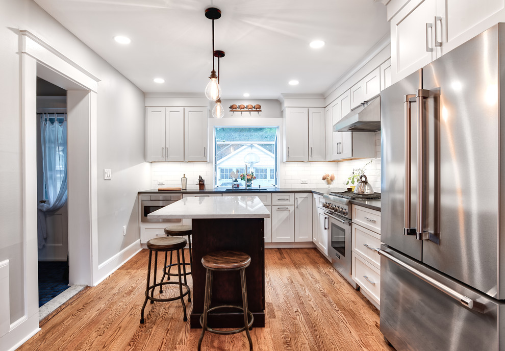 Photo of a mid-sized country l-shaped kitchen pantry in New York with a drop-in sink, beaded inset cabinets, white cabinets, white splashback, subway tile splashback, stainless steel appliances, painted wood floors, with island, brown floor, marble benchtops and black benchtop.