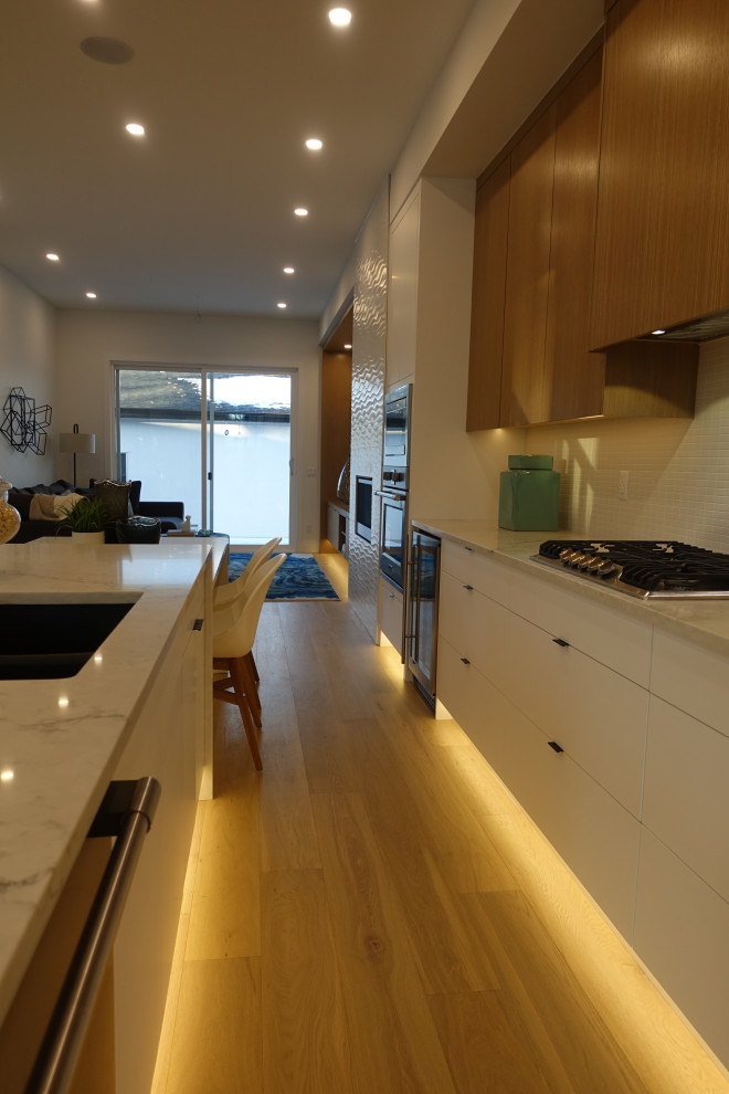 Small transitional single-wall eat-in kitchen in Calgary with a double-bowl sink, flat-panel cabinets, white cabinets, quartz benchtops, white splashback, stone tile splashback, coloured appliances, medium hardwood floors, multiple islands, white floor, white benchtop and recessed.