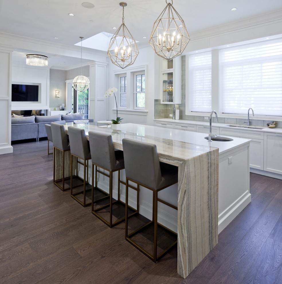 Photo of a transitional kitchen in Orlando with an undermount sink, recessed-panel cabinets, white cabinets, grey splashback, panelled appliances, dark hardwood floors, with island, brown floor and white benchtop.