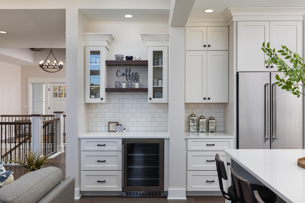 Example of a mid-sized beach style medium tone wood floor and brown floor eat-in kitchen design in Grand Rapids with a farmhouse sink, recessed-panel cabinets, white cabinets, quartzite countertops, white backsplash, subway tile backsplash, stainless steel appliances, an island and white countertops