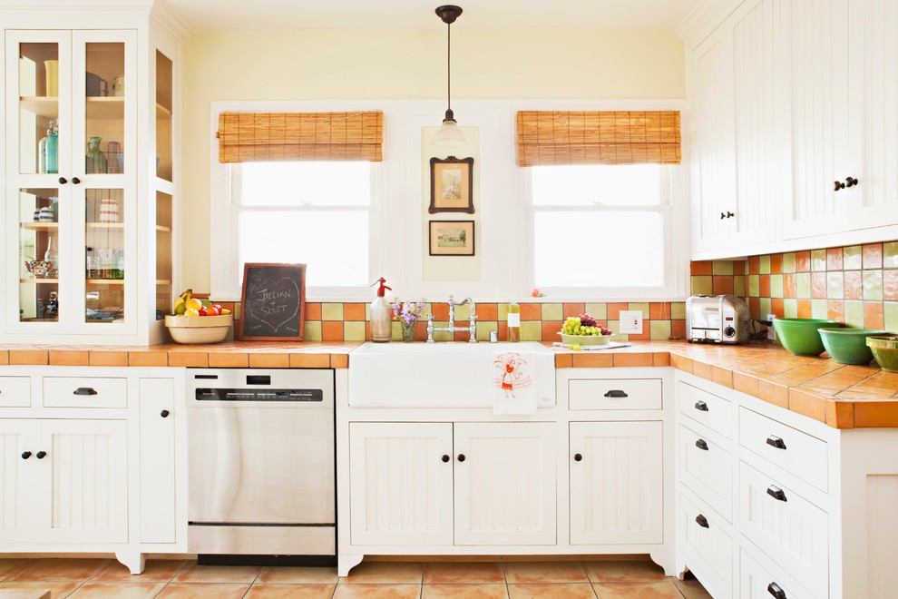 Design ideas for a mid-sized traditional l-shaped eat-in kitchen in Los Angeles with beaded inset cabinets, white cabinets, a farmhouse sink, tile benchtops, terra-cotta splashback, stainless steel appliances, terra-cotta floors and multi-coloured splashback.