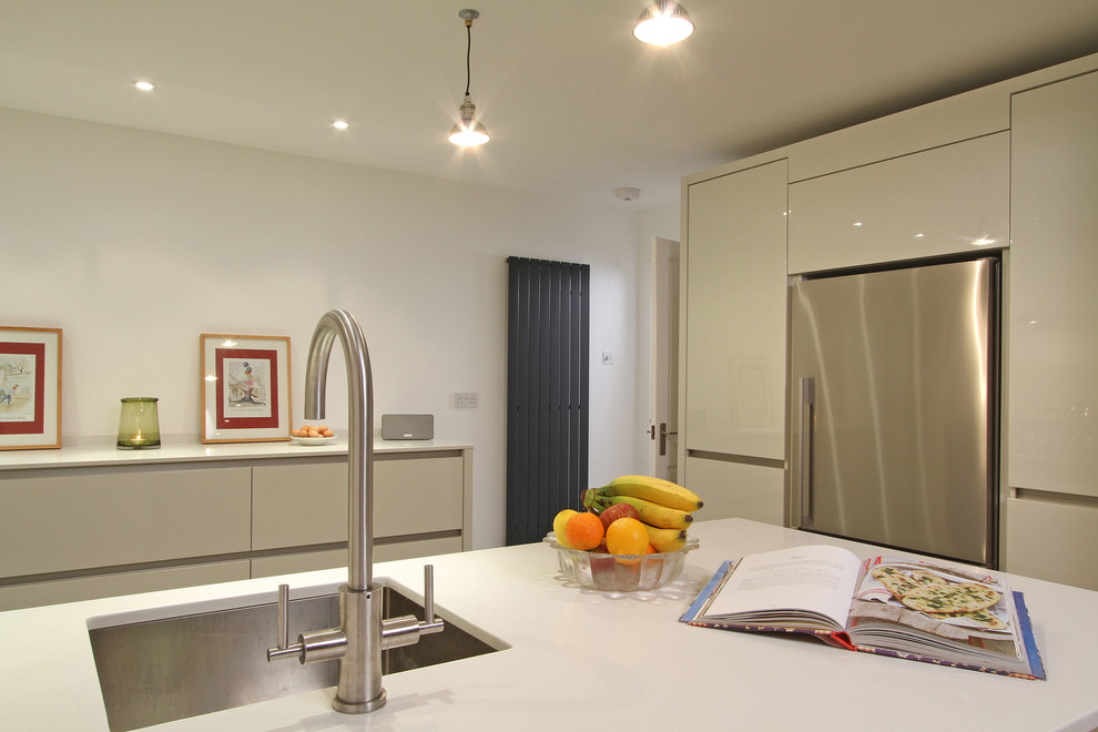 Mid-sized modern u-shaped eat-in kitchen in Hampshire with a single-bowl sink, flat-panel cabinets, white cabinets, quartz benchtops, beige splashback, glass sheet splashback, coloured appliances and a peninsula.