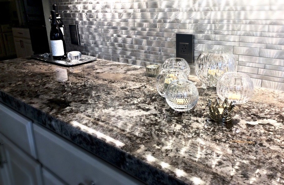 Example of a mid-sized transitional l-shaped travertine floor eat-in kitchen design in Houston with a farmhouse sink, raised-panel cabinets, white cabinets, granite countertops, metallic backsplash, metal backsplash, stainless steel appliances and an island