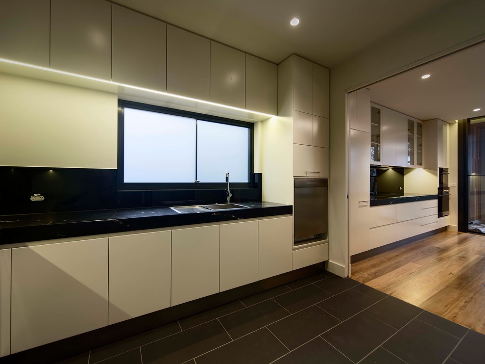 Photo of a large contemporary galley open plan kitchen in Melbourne with an undermount sink, flat-panel cabinets, white cabinets, marble benchtops, black splashback, glass sheet splashback, stainless steel appliances, light hardwood floors and multiple islands.