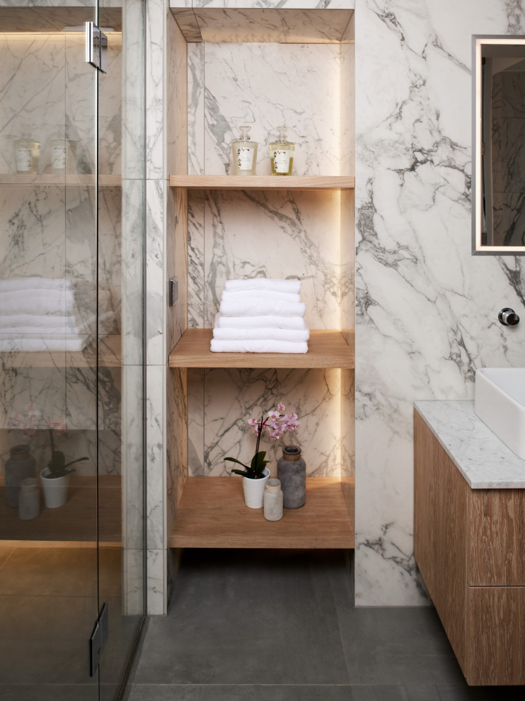 This is an example of a large contemporary ensuite bathroom in Other with flat-panel cabinets, light wood cabinets, a freestanding bath, a walk-in shower, a wall mounted toilet, grey tiles, marble tiles, multi-coloured walls, ceramic flooring, a pedestal sink, grey floors, a hinged door, a feature wall, double sinks and a floating vanity unit.
