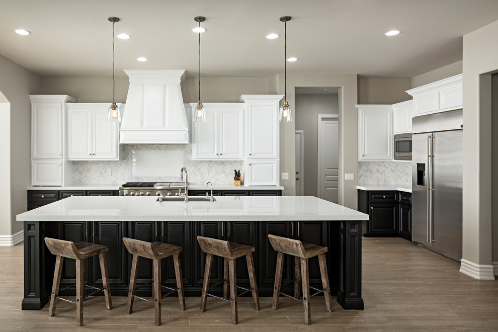 Example of a large transitional l-shaped light wood floor and brown floor open concept kitchen design in Phoenix with an undermount sink, raised-panel cabinets, black cabinets, quartz countertops, white backsplash, marble backsplash, stainless steel appliances and an island