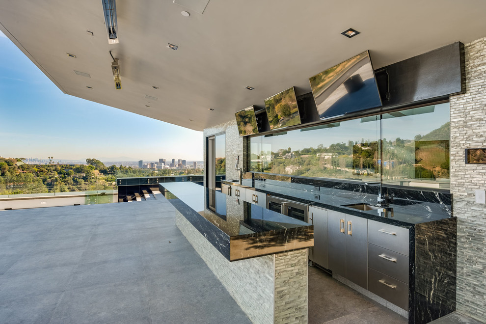 Expansive contemporary u-shaped seated home bar in Los Angeles with an undermount sink, flat-panel cabinets, grey cabinets, onyx benchtops, grey splashback, glass sheet splashback, concrete floors, grey floor and black benchtop.