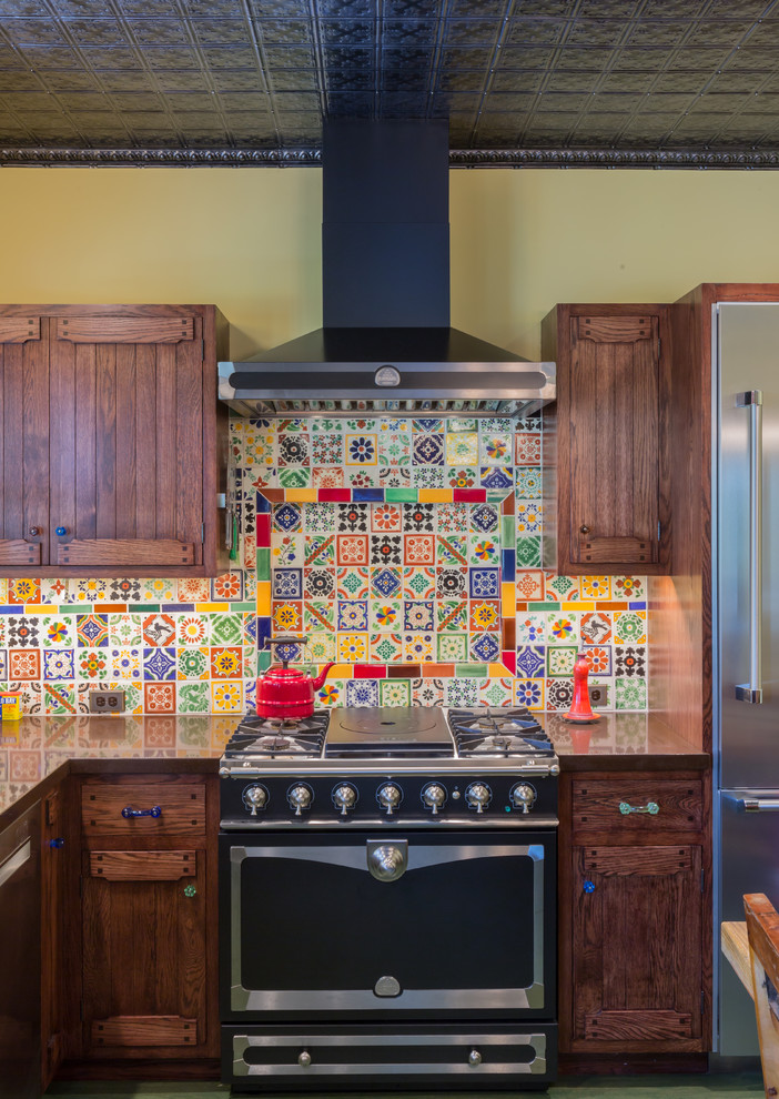 This is an example of an eclectic l-shaped separate kitchen in San Francisco with a single-bowl sink, flat-panel cabinets, dark wood cabinets, solid surface benchtops, multi-coloured splashback, mosaic tile splashback, stainless steel appliances, medium hardwood floors, no island, green floor and black benchtop.