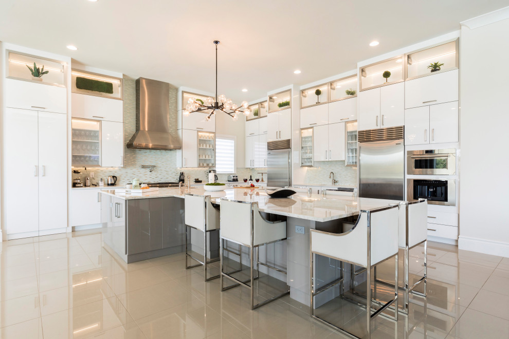This is an example of an expansive contemporary l-shaped kitchen in Orlando with an undermount sink, flat-panel cabinets, white cabinets, quartz benchtops, green splashback, mosaic tile splashback, stainless steel appliances, porcelain floors, with island, beige floor and white benchtop.