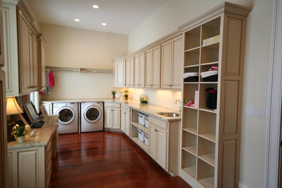 Inspiration for a large mediterranean u-shaped utility room in Cleveland with an undermount sink, raised-panel cabinets, beige cabinets, granite benchtops, beige walls, dark hardwood floors, a side-by-side washer and dryer and red floor.