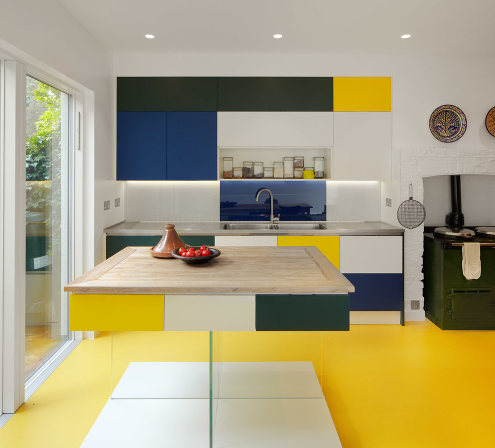 Photo of a mid-sized contemporary kitchen in London with a double-bowl sink, flat-panel cabinets, stainless steel benchtops, blue splashback, glass sheet splashback, coloured appliances, linoleum floors, with island and yellow floor.