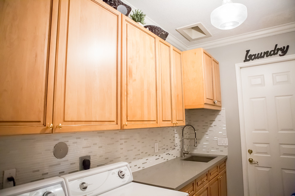 Photo of a mid-sized traditional galley laundry cupboard in Miami with an undermount sink, raised-panel cabinets, light wood cabinets, limestone benchtops, grey walls, a side-by-side washer and dryer and grey benchtop.