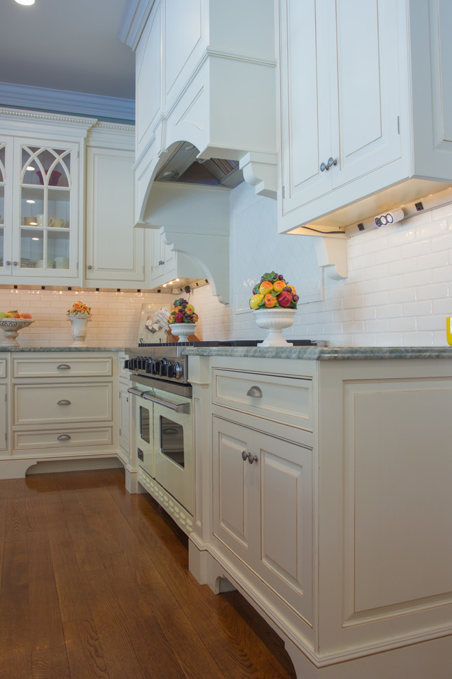 Mid-sized traditional l-shaped eat-in kitchen in New York with a farmhouse sink, white cabinets, granite benchtops, white splashback, subway tile splashback, stainless steel appliances and medium hardwood floors.