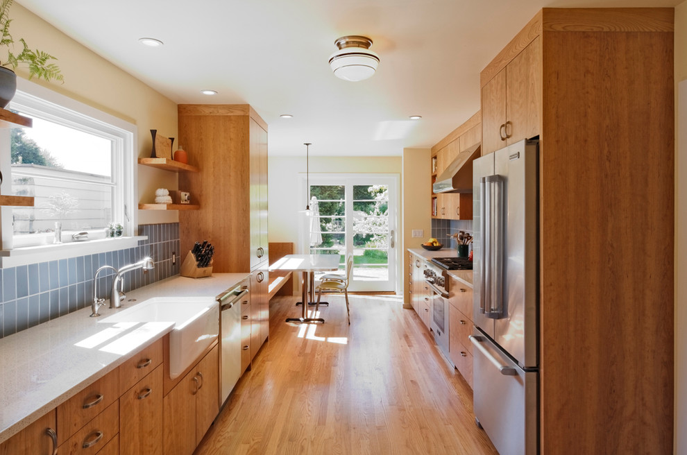 Design ideas for a modern galley eat-in kitchen in Portland with a farmhouse sink, medium wood cabinets, recycled glass benchtops, blue splashback, subway tile splashback, stainless steel appliances, flat-panel cabinets and light hardwood floors.