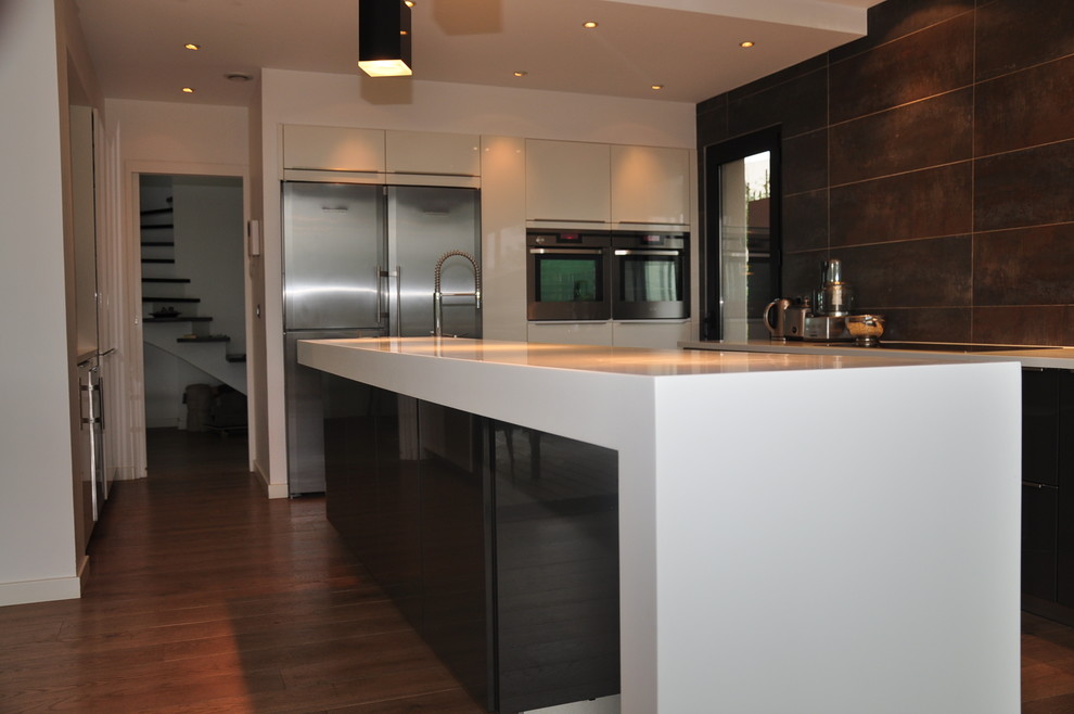 Photo of a large contemporary galley open plan kitchen in Montpellier with an integrated sink, black cabinets, white splashback, stainless steel appliances, medium hardwood floors, with island, solid surface benchtops and ceramic splashback.