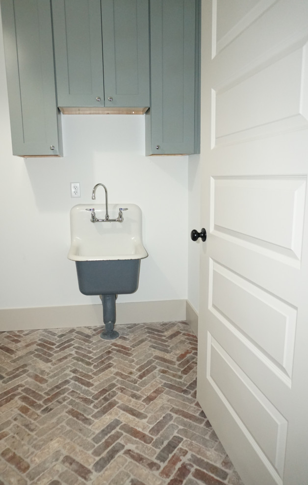 This is an example of a mid-sized country u-shaped dedicated laundry room in Other with flat-panel cabinets, grey cabinets, white walls, brick floors, a side-by-side washer and dryer, brown floor and an integrated sink.