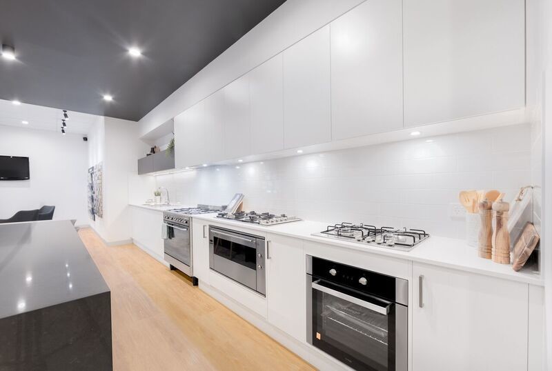 Large contemporary galley kitchen in Wollongong with a double-bowl sink, white cabinets, quartz benchtops, white splashback, porcelain splashback, stainless steel appliances, vinyl floors and with island.