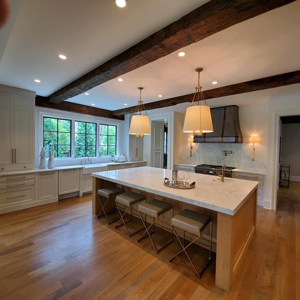Photo of a mid-sized transitional u-shaped kitchen in Atlanta with a farmhouse sink, beaded inset cabinets, beige cabinets, wood benchtops, white splashback, marble splashback, light hardwood floors, with island, white benchtop and exposed beam.