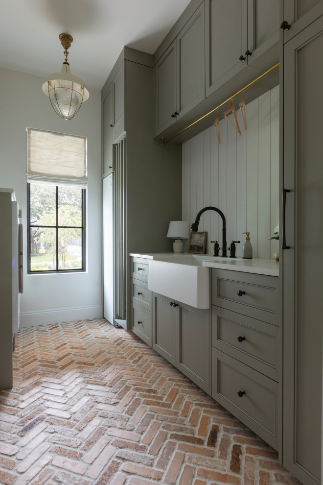 Inspiration for a transitional brick floor laundry room remodel in San Francisco with a farmhouse sink, recessed-panel cabinets, green cabinets, shiplap backsplash, white walls, a side-by-side washer/dryer and white countertops
