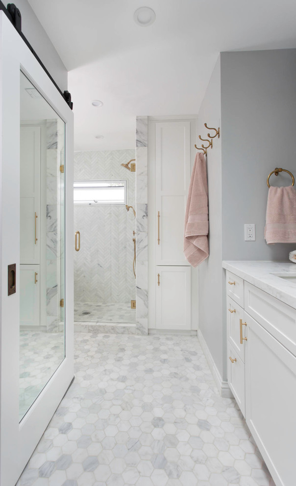 Photo of a mid-sized transitional master bathroom in Denver with recessed-panel cabinets, white cabinets, an alcove shower, a one-piece toilet, gray tile, glass tile, grey walls, marble floors, an undermount sink, marble benchtops, white floor, a hinged shower door and white benchtops.