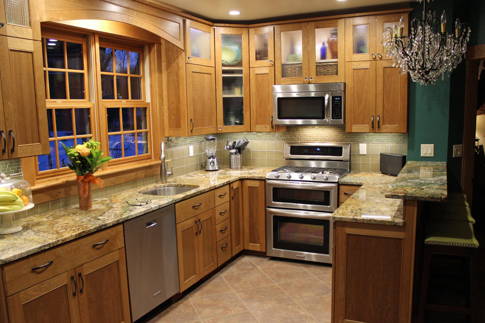 Example of a mid-sized arts and crafts l-shaped ceramic tile enclosed kitchen design with a single-bowl sink, glass-front cabinets, medium tone wood cabinets, granite countertops, green backsplash, glass tile backsplash, stainless steel appliances and a peninsula