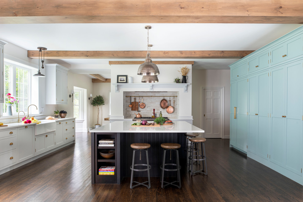 This is an example of a large u-shaped eat-in kitchen in Boston with a farmhouse sink, beaded inset cabinets, quartz benchtops, multi-coloured splashback, porcelain splashback, stainless steel appliances, dark hardwood floors, with island, brown floor, white benchtop and exposed beam.