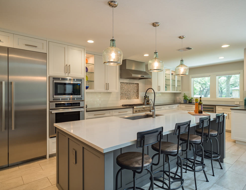 This is an example of a mid-sized contemporary l-shaped eat-in kitchen in Austin with a farmhouse sink, shaker cabinets, white cabinets, quartzite benchtops, white splashback, porcelain splashback, stainless steel appliances, ceramic floors, with island and beige floor.