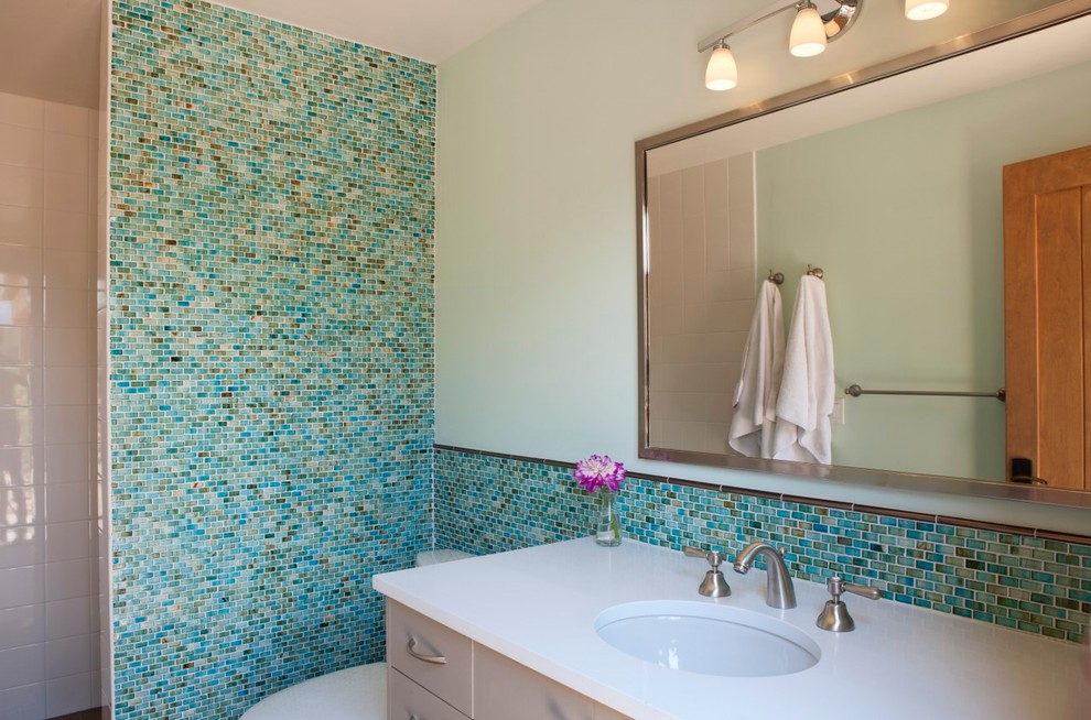 Inspiration for a mid-sized country 3/4 bathroom in Albuquerque with flat-panel cabinets, grey cabinets, an alcove shower, a two-piece toilet, multi-coloured tile, mosaic tile, green walls, an undermount sink and solid surface benchtops.