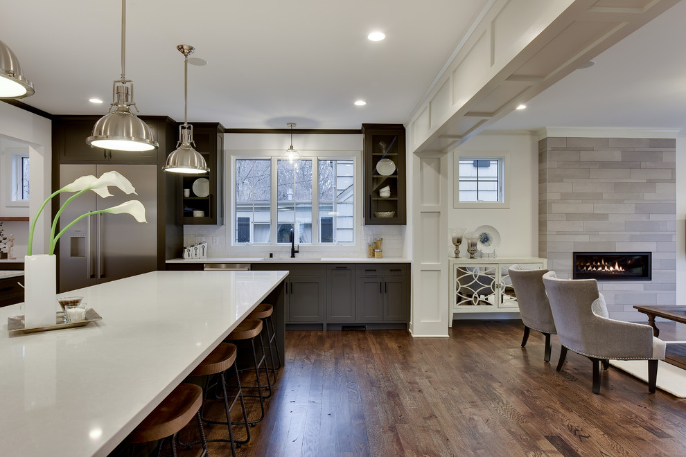 This is an example of a large transitional l-shaped eat-in kitchen in Minneapolis with an undermount sink, shaker cabinets, grey cabinets, white splashback, stainless steel appliances, dark hardwood floors, with island and brown floor.