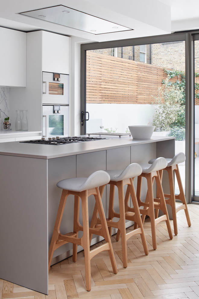 Inspiration for a mid-sized eat-in kitchen in London with a drop-in sink, flat-panel cabinets, grey cabinets, laminate benchtops, white splashback, marble splashback, stainless steel appliances, light hardwood floors, with island, beige floor and grey benchtop.