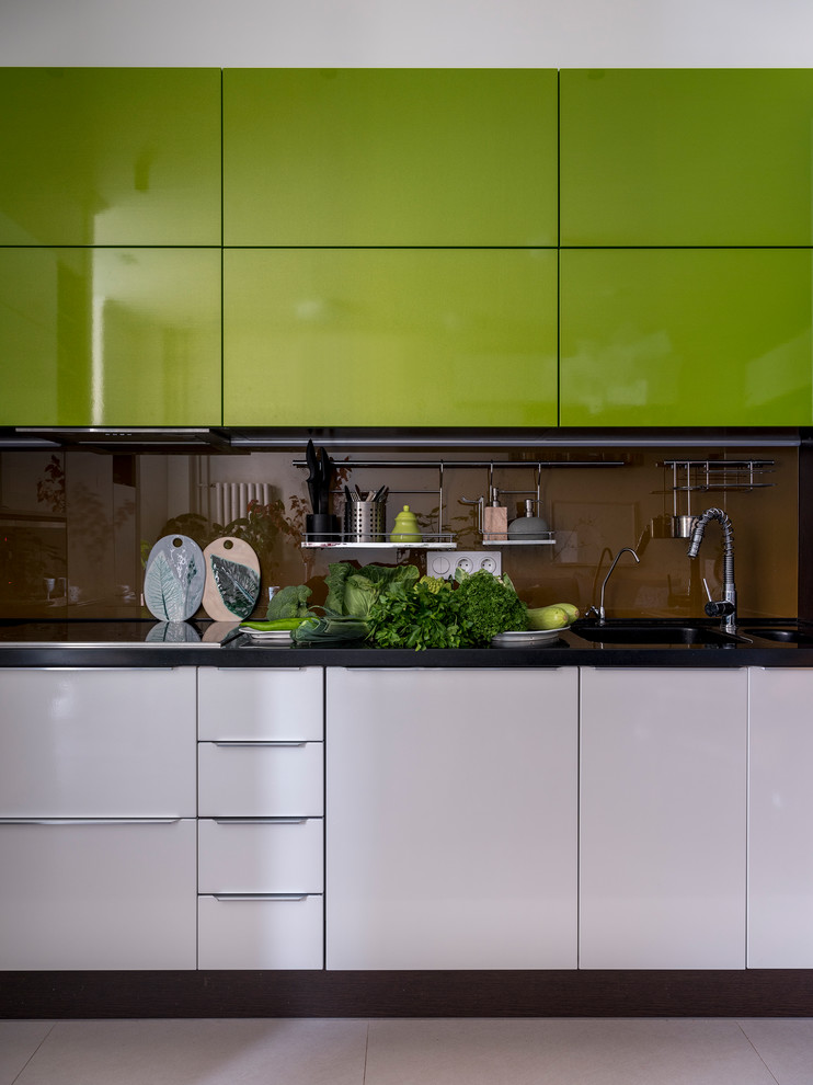 Photo of a mid-sized eclectic single-wall open plan kitchen in Moscow with a double-bowl sink, flat-panel cabinets, green cabinets, brown splashback, glass sheet splashback, stainless steel appliances, dark hardwood floors, brown floor and black benchtop.