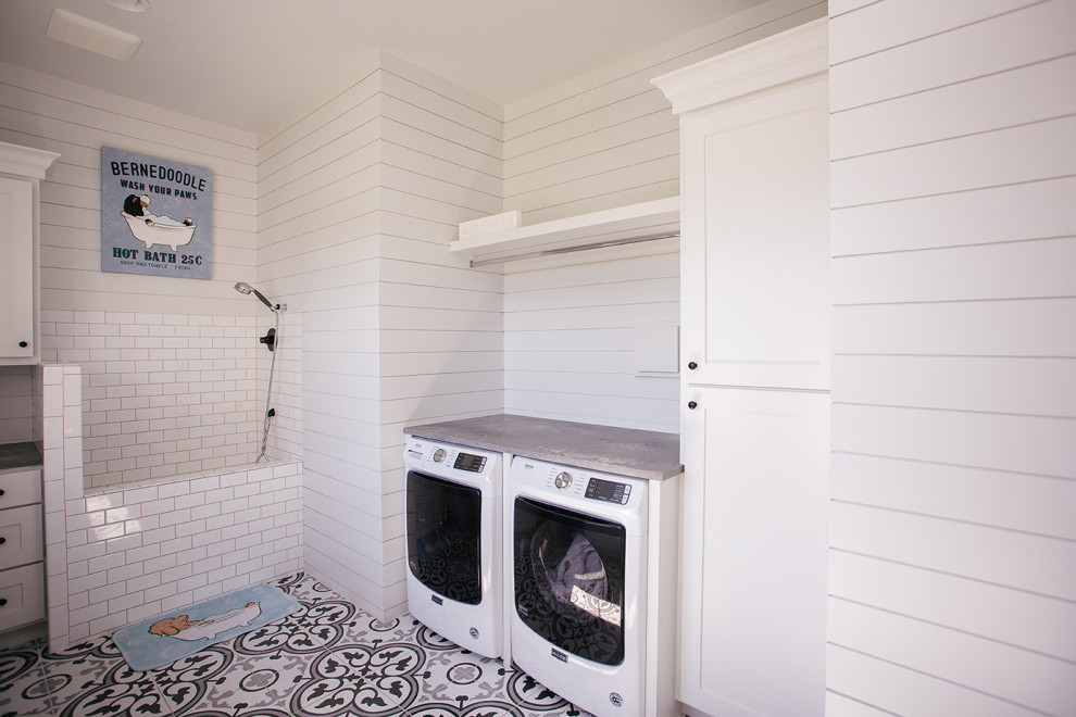 This is an example of a mid-sized country laundry room in Portland with a drop-in sink, white cabinets, window splashback, white walls, a side-by-side washer and dryer, multi-coloured floor and grey benchtop.