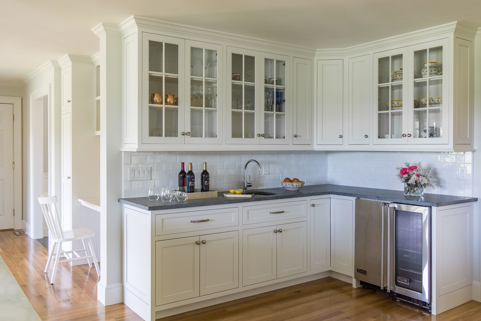 Design ideas for a mid-sized country l-shaped eat-in kitchen in Boston with a farmhouse sink, recessed-panel cabinets, white cabinets, granite benchtops, subway tile splashback, stainless steel appliances, medium hardwood floors and with island.