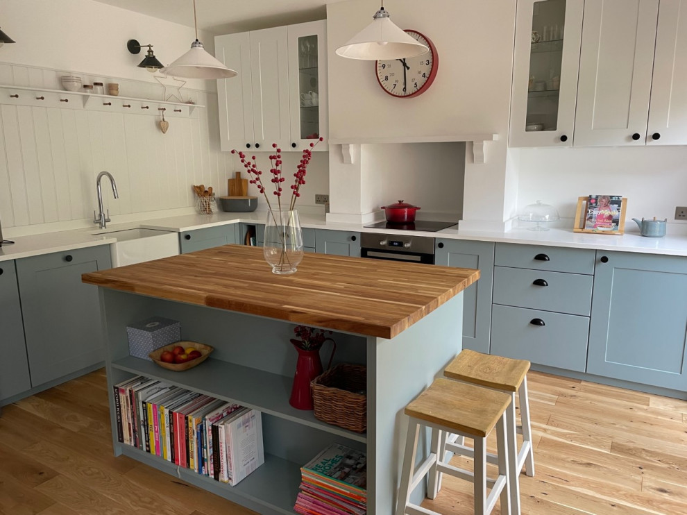 Eat-in kitchen - large traditional l-shaped light wood floor eat-in kitchen idea in London with a farmhouse sink, shaker cabinets, blue cabinets, solid surface countertops, white backsplash, stainless steel appliances, an island and white countertops