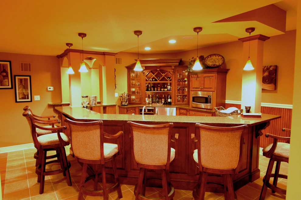 Photo of a mid-sized traditional single-wall seated home bar in New York with a drop-in sink, raised-panel cabinets, medium wood cabinets, granite benchtops and ceramic floors.
