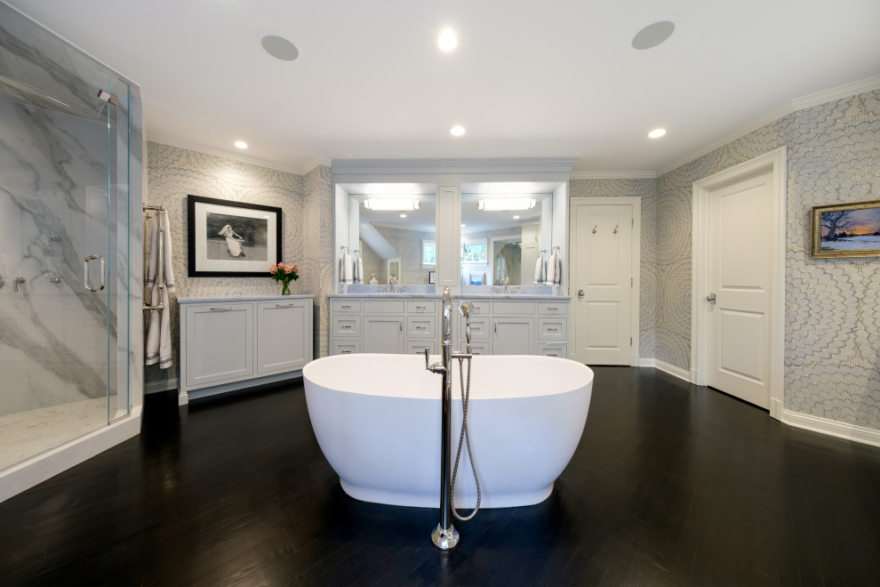 Expansive transitional master bathroom in New York with recessed-panel cabinets, grey cabinets, a freestanding tub, a double shower, multi-coloured walls, dark hardwood floors, an undermount sink, marble benchtops, a hinged shower door, blue benchtops, an enclosed toilet, a double vanity, a built-in vanity and wallpaper.