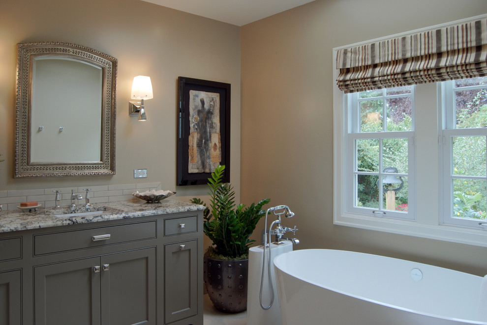 Design ideas for a mid-sized traditional bathroom in Portland with beaded inset cabinets, brown cabinets, a freestanding tub, an undermount sink, granite benchtops, ceramic tile, beige walls, porcelain floors and beige tile.