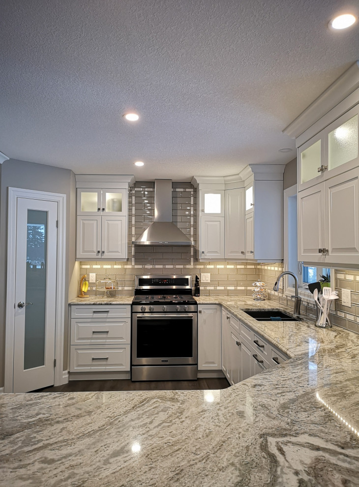 Mid-sized transitional u-shaped light wood floor and brown floor enclosed kitchen photo in Toronto with an undermount sink, raised-panel cabinets, white cabinets, granite countertops, beige backsplash, glass tile backsplash, stainless steel appliances, a peninsula and gray countertops