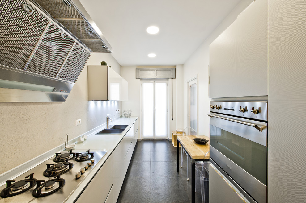 Mid-sized contemporary single-wall eat-in kitchen in Rome with a double-bowl sink, flat-panel cabinets, white cabinets, solid surface benchtops, stainless steel appliances and slate floors.