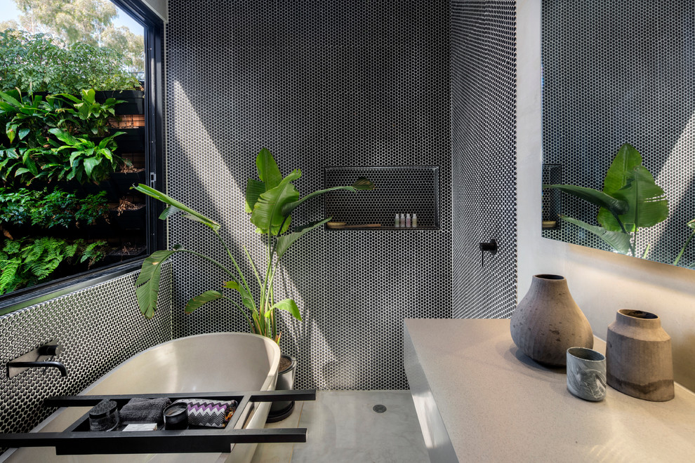 Photo of a mid-sized contemporary master bathroom in Melbourne with a freestanding tub, an open shower, a wall-mount toilet, black tile, mosaic tile, concrete floors and marble benchtops.