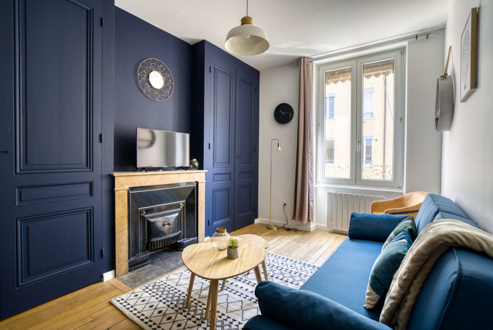 Exemple d'un petit salon moderne ouvert avec un mur bleu, parquet clair, une cheminée standard, un manteau de cheminée en pierre de parement et un téléviseur indépendant.