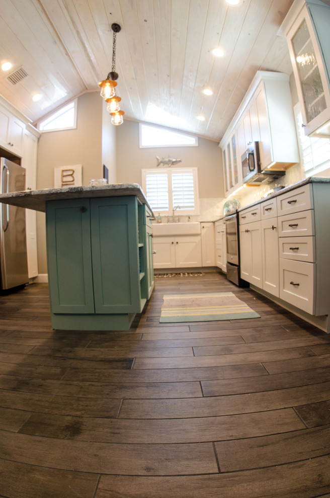 Inspiration for a mid-sized beach style u-shaped open plan kitchen in Tampa with a farmhouse sink, white cabinets, white splashback, stainless steel appliances, with island, shaker cabinets, marble benchtops, porcelain splashback and dark hardwood floors.